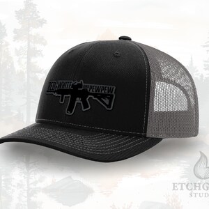 May include: A black and gray trucker hat with the text "RED WHITE AND PEWPEW" and a graphic of a rifle. The hat has a mesh back and a curved brim. The hat is a baseball cap style.