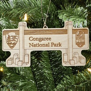 May include: Wooden ornament featuring the Congaree National Park sign. The ornament includes the National Park Service logo and the park name. The design is light brown and hangs from a string, perfect for a Christmas tree.