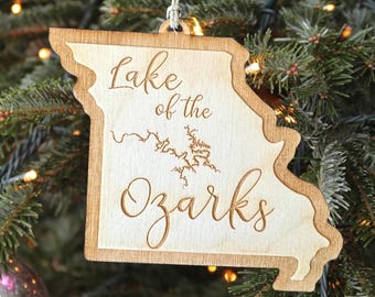 May include: A wooden Christmas ornament shaped like the state of Missouri with the text "Lake of the Ozarks" and a map of the lake inside the state outline.