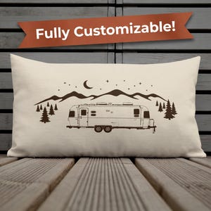 May include: Beige rectangular cushion featuring a brown illustration of a travel trailer, mountains, trees, moon, and stars. The text "Fully Customizable!" is displayed on a brown banner above the cushion.