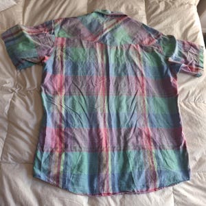 K&ouml;nnte beinhalten: Ein kurz&auml;rmeliges Hemd mit einem pastellfarbenen Karomuster in Rosa, Blau, Gr&uuml;n und Lila. Das Hemd hat eine Knopfleiste und einen klassischen Kragen. Der Stoff scheint leicht zu sein, geeignet f&uuml;r w&auml;rmeres Wetter.
