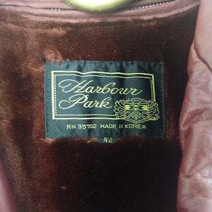 May include: Close-up of a vintage burgundy coat interior. The coat features a dark brown faux fur lining and a label that reads "Harbour Park" with "Made in Korea" and size "42". The coat is hanging on a gold-colored hanger.