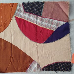 May include: A patchwork quilt block with various fabrics in shades of brown, red, beige, blue, and black. The fabrics are sewn together in a curved pattern, creating a unique and artistic design.