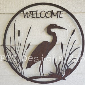 May include: A rusty metal welcome sign with a silhouette of a heron standing in reeds. The sign reads "Welcome".