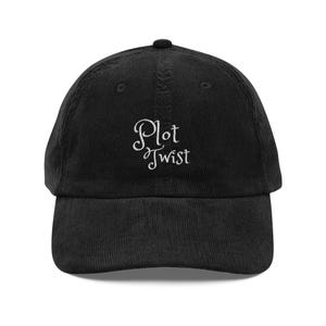 Puede incluir: Gorra de béisbol negra de pana con visera curva. La gorra presenta el texto bordado "Plot Twist" en blanco, con una fuente cursiva. El sombrero tiene un ajuste estructurado y un botón superior.