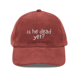 Peut inclure: Casquette de baseball en velours côtelé rouge brique avec une visière incurvée. Le texte brodé "is he dead yet?" en blanc est centré sur le devant. Le chapeau a un design classique à six panneaux avec un bouton supérieur.