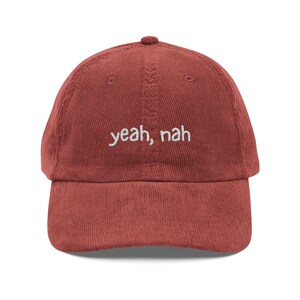 Könnte beinhalten: Ziegelrotes Cord-Baseballcap mit gebogenem Schirm. Der Schriftzug "yeah, nah" ist in Weiß auf die Vorderseite gestickt. Die Kappe hat ein sechsteiliges Design mit einem Knopf oben.