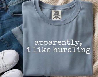Może przedstawiać: Niebieska koszulka z białym napisem "apparently, i like hurdling". Koszulka jest połączona z niebieskimi dżinsami i białymi trampkami. Koszulka ma metkę Comfort Colors.