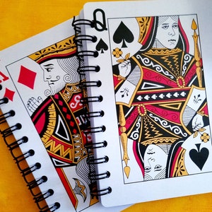 A 5 x 7 notebook with covers made from oversized playing cards. Traditional red black and gold face card motif. Black spiral binding with 60 blank pages of 80-pound paper. Clear lid box with stretch cord, gift tag and coordinating red pen. Great gift