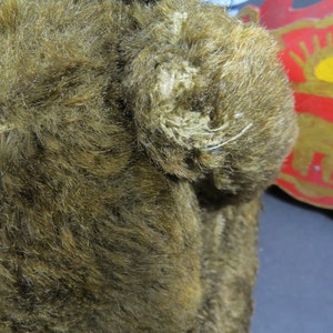 May include: A brown plush teddy bear with a green ribbon around its neck. The bear's fur is worn and has some loose threads.