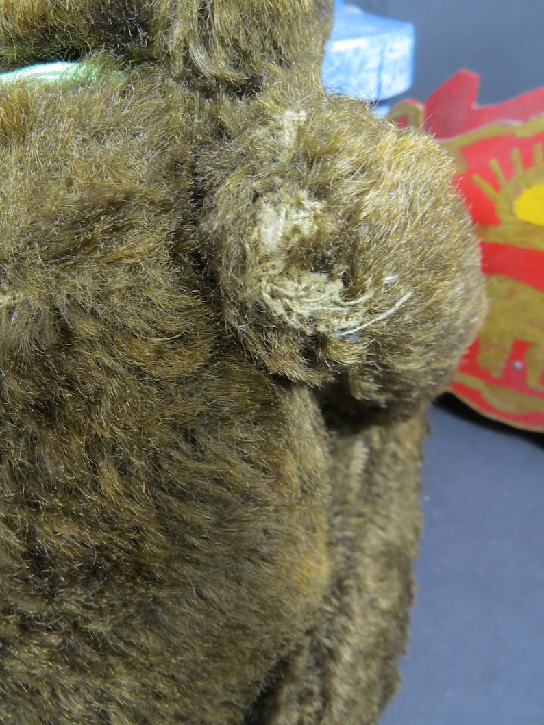 May include: A brown plush teddy bear with a green ribbon around its neck. The bear's fur is worn and has some loose threads.