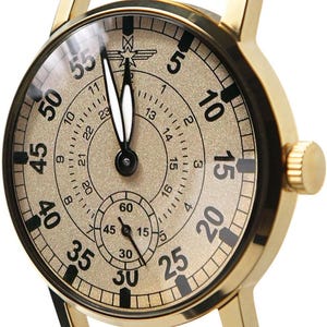 May include: Gold-toned wristwatch with a mesh band. The watch face is beige with black numerals and hands. A smaller dial is at the bottom. The watch has a gold-colored case and a mesh band.