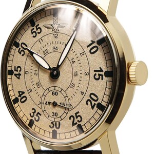 May include: Gold-toned wristwatch with a black leather band. The watch face features black numerals and hands against a gold background. The watch has a small seconds dial and a 24-hour indicator.