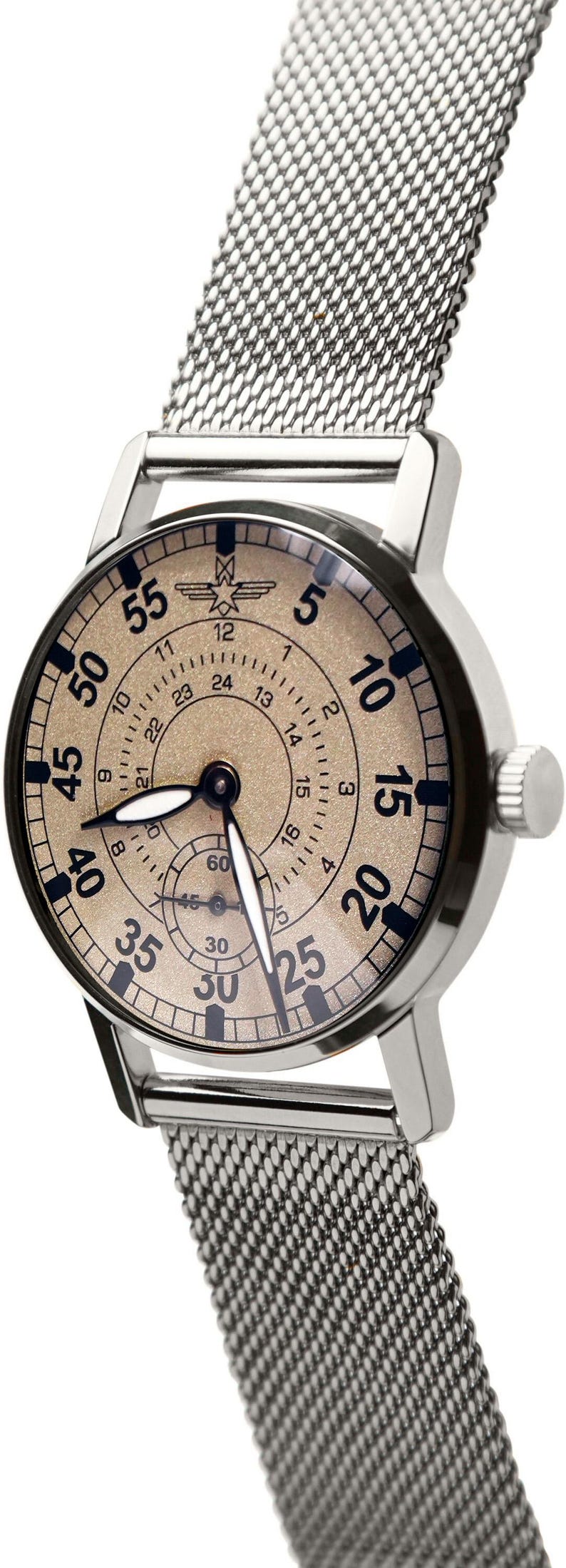 May include: Silver-toned wristwatch with a mesh band. The watch face is tan with black numerals and hands. The watch has a small seconds dial and a 24-hour clock. The band is made of a fine, woven metal.