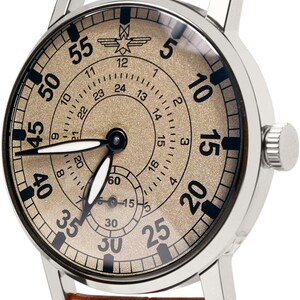 May include: A silver-cased wristwatch with a tan face and brown leather band. The watch face features black numerals and a subdial. The brown leather band is stitched with orange thread.