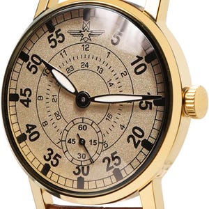 May include: A gold-toned wristwatch with a brown leather band. The watch face features black numerals and a subdial. The band is stitched with orange thread. The watch has a classic, vintage aesthetic.