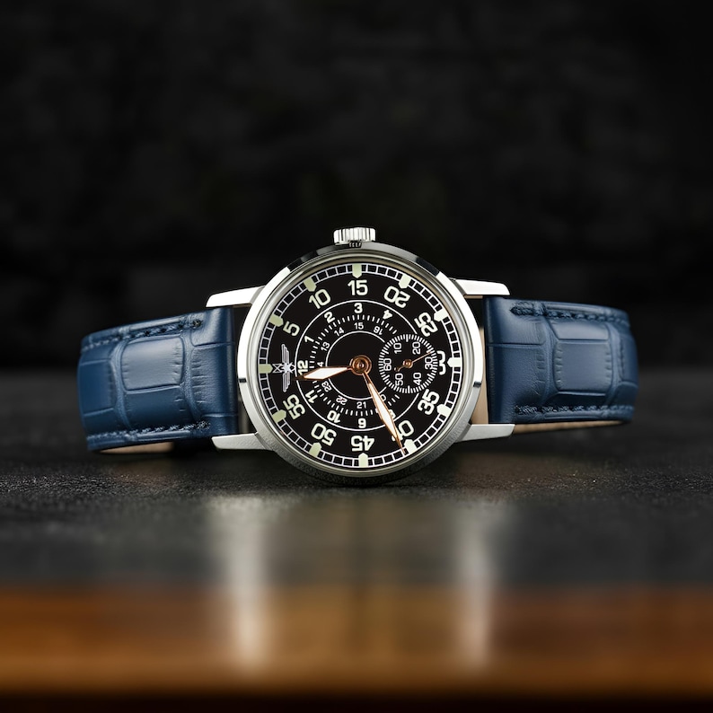 May include: A silver-cased wristwatch with a black face and white numerals. The watch features a small seconds dial and a blue leather strap. The watch face displays the numbers 5, 10, 15, 20, 25, 30, 35, 40, 45, 50, and 55.