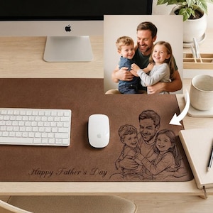 Puede incluir: Un tapete de escritorio de cuero marrón con una ilustración grabada con láser de un padre abrazando a dos niños, con el texto "Happy Father's Day" inscrito debajo. El tapete está colocado sobre un escritorio con teclado y ratón.