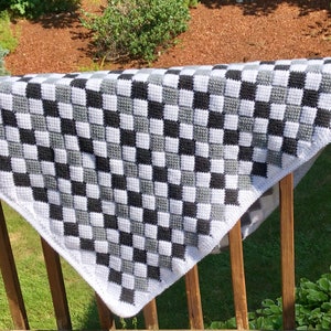 May include: A black, white and grey checkered crochet blanket hanging on a wooden railing.