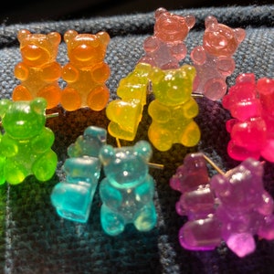 May include: A set of gummy bear earrings in various colors, including green, orange, yellow, pink, and purple. Each pair features two gummy bear charms.