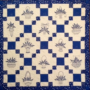May include: A blue and white quilt with a checkered pattern. The quilt is decorated with embroidered baskets of flowers.