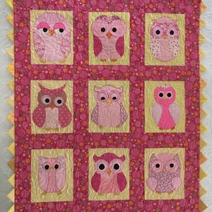 Puede incluir: Una colcha rosa y amarilla con un patrón de nueve búhos. Los búhos son todos de diseños diferentes y tienen detalles rosas, blancos y negros.