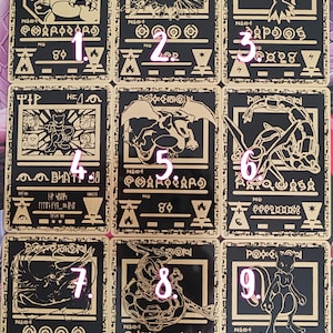 Peut inclure: Neuf cartes à collectionner à bordure dorée avec diverses illustrations de Pokémon sur fond noir. Chaque carte présente des illustrations, des symboles et du texte uniques, dont le mot "Pokémon" en haut. Les cartes sont disposées en grille 3x3.