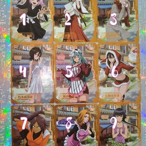 May include: A collection of nine rectangular trading cards featuring anime characters from the series Bleach, each with a gold-toned border and a background depicting a traditional Japanese street scene, numbered one through nine in pink text.