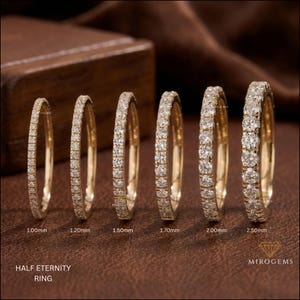 Peut inclure: Six bagues demi-éternité en or alignées, chacune sertie d'une ligne de diamants ronds. Les bagues sont étiquetées avec des largeurs de 1,00 mm, 1,20 mm, 1,50 mm, 1,70 mm, 2,00 mm et 2,50 mm. Le texte "HALF ETERNITY RING" est inscrit en bas à gauche.