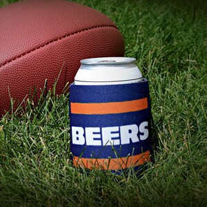 May include: A blue and orange can cooler with the word "BEERS" in white letters. The cooler is sitting on green grass next to a brown football.