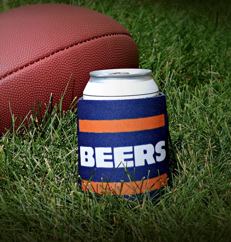 May include: A blue and orange can cooler with the word "BEERS" in white letters. The cooler is sitting on green grass next to a brown football.