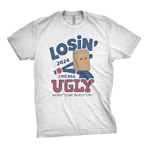 May include: White t-shirt with blue and red text that says "Losin' 2024 Chicago Ugly Worst Team in History". A cartoon figure with a paper bag over its head is holding a baseball bat.