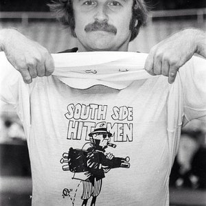 Puede incluir: Una fotograf&iacute;a en blanco y negro de una persona que lleva una gorra de b&eacute;isbol y una camiseta blanca con el texto "South Side Hitmen" y una ilustraci&oacute;n de dibujos animados de una persona que sostiene una bolsa de bates.