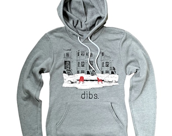 May include: A grey hooded sweatshirt with a black and white illustration of a snowy city street scene with two red chairs. The text "dibs." is printed below the illustration.