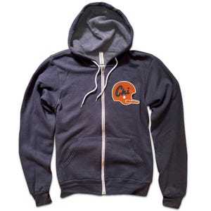May include: A navy blue zip-up hoodie with a white zipper and drawstrings. An orange and white patch of a football helmet with the word "Chi" is on the chest. The hoodie has a hood and two front pockets.