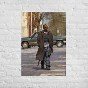 May include: A person with short hair wearing a long dark brown trench coat over a blue shirt and blue jeans, walking on a paved street. In the background, a dark teal pickup truck is parked near trees and a building under a bright sky.