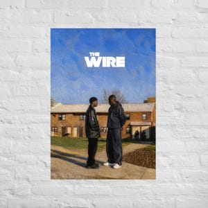 May include: A vertical poster featuring the text THE WIRE in white capital letters against a blue sky. Two individuals stand facing each other in front of a brick building complex. One wears a black jacket and pants, the other a dark tracksuit.