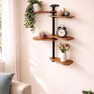 May include: A wall-mounted shelving unit featuring a central black metal pole with five staggered, rounded wooden shelves. The shelves hold a potted trailing plant, a glass bowl with decorative items, a black alarm clock, and a vase with tulips.