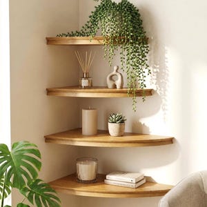 Op de afbeelding: Vier lichtbruine houten hoekplanken gemonteerd aan een muur. De bovenste plank bevat een hangende groene plant. De tweede plank is voorzien van een geurstokjesdiffuser en een klein abstract beeldje. De derde plank toont een kaars.