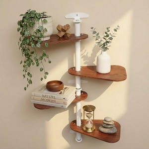 May include: A wall-mounted shelving unit featuring a central white vertical pole with four asymmetrical, dark wood-toned shelves. The shelves hold a trailing green plant in a white pot, a wooden object, books titled Nature Modern, a white vase, and an hourglass.