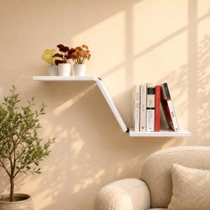 May include: A white, two-tiered wall-mounted shelf with an angled connecting piece. The upper level holds three small potted plants, while the lower level displays a row of books with various colored spines, including white, red, and black.