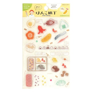 Op de afbeelding: Een vel met doorzichtige stempels met diverse Japanse voedselillustraties, waaronder sushi, bento-box-onderdelen en rijstballen. De verpakking bevat de tekst "Hanko Yokocho" en "Clear Stamp" met kleurrijke afbeeldingen van etenswaren.