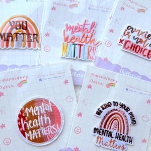 May include: A collection of colorful embroidered patches with mental health themes. The patches feature phrases like "You Matter," "Mental Health Matters," and "Anxiety is Not a Choice." Each patch is on a backing card with the "fluffstuff" logo.