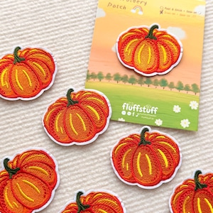 May include: Embroidered pumpkin patches in orange and yellow with green stems and white borders. The patches are arranged on a textured, off-white surface. One patch is attached to a card with the text "Embroidery Patch".