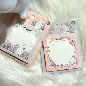 以下が含まれることがあります： ムーミンのテーマの付箋2冊。1冊はピンクの縁取りのグレー、もう1冊はグレーの縁取りのピンクです。各パッドには、花に囲まれたムーミンのキャラクターイラストが描かれています。パッドには「Moomin」の文字が印刷されています。