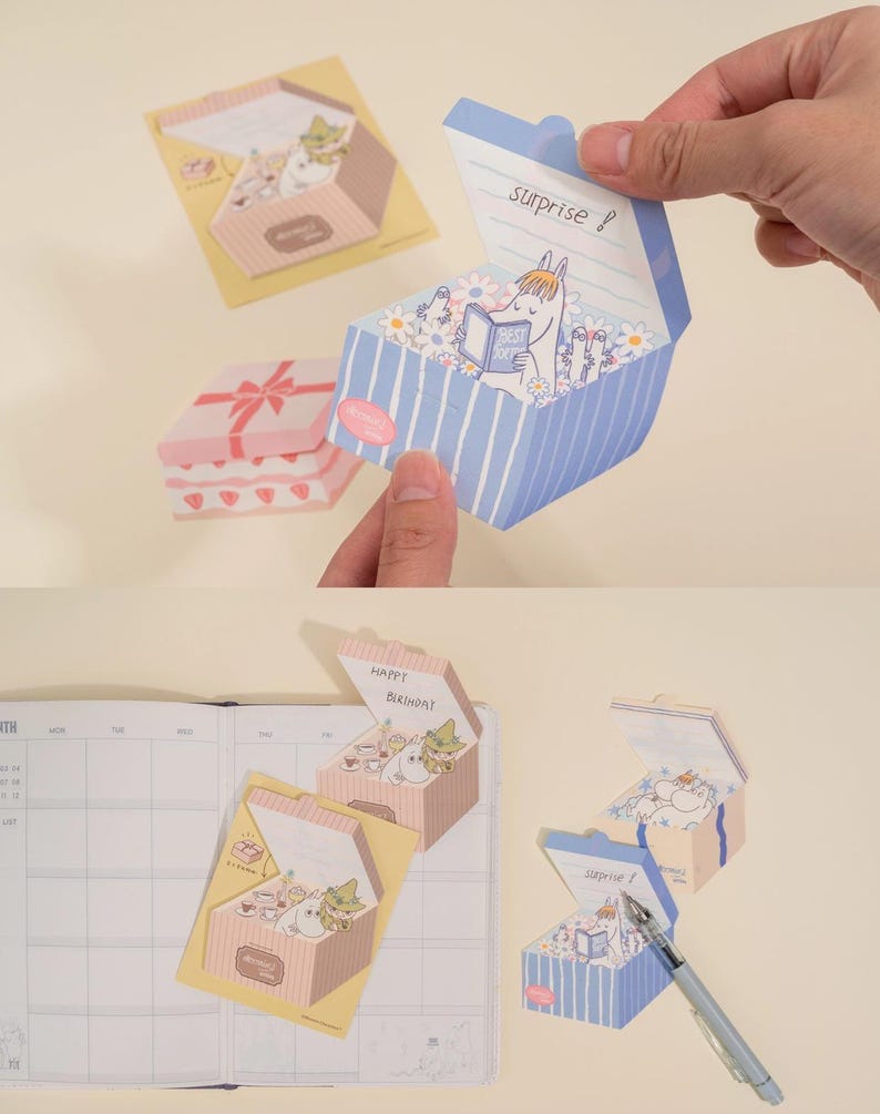 May include: A collection of decorative paper boxes with pop-up designs. One box is blue with white stripes and the word "surprise" on the lid. Another is pink with a bow design. The boxes feature cartoon characters and floral elements.
