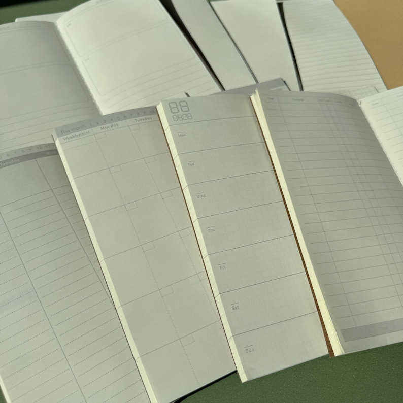 May include: A collection of open planners and notebooks with off-white pages featuring various layouts including weekly calendars, daily schedules, and lined sections. The pages display printed text for days of the week and grid patterns in gray ink.