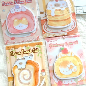 Puede incluir: Cuatro notas adhesivas coloridas con temática de gatos. Las notas presentan ilustraciones de gatos como postres, incluyendo un rollo de gatito de melocotón, un gato muffin de cereza, un gato tostada de cacao y un gato crema de fresa. Cada nota está empaquetada con el texto "MO-CARD" y "30PCS".