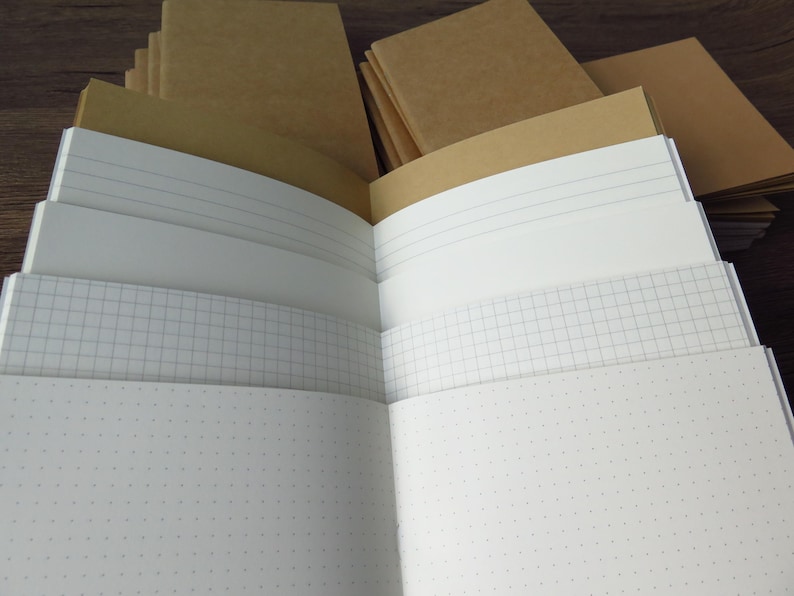 May include: A collection of notebooks with plain brown kraft paper covers. The notebooks are open to reveal various interior page styles, including white pages with horizontal lines, white pages with a grid pattern, and white pages with a dot grid.