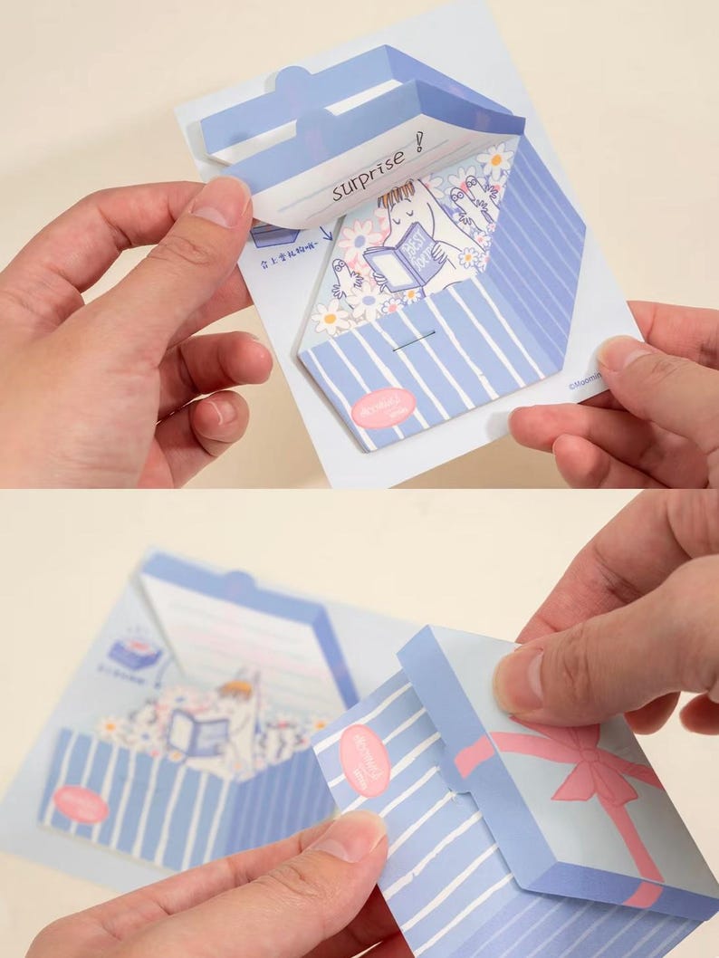May include: A light blue and white striped paper gift box with a pink bow. The box is being opened to reveal a cartoon illustration of a character reading a book. The word "surprise!" is written on the inside flap.